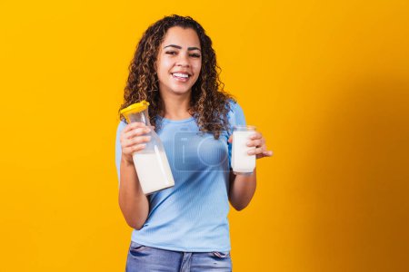 Photo for Young girl drinking a glass of milk and holding the full bottle. - Royalty Free Image