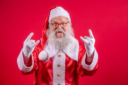 Foto de Santa Claus haciendo rock n roll signo con las manos y el fondo rojo. - Imagen libre de derechos