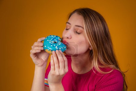 Téléchargez les photos : Portrait d'une jeune fille blonde mangeant un délicieux beignets colorés. - en image libre de droit