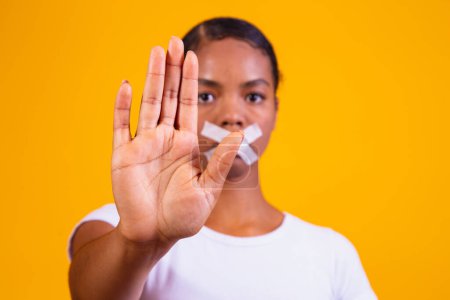 Foto de Mujer negra sobre fondo amarillo con la boca cerrada en silencio. Concepto de prejuicio, abuso y racismo - Imagen libre de derechos