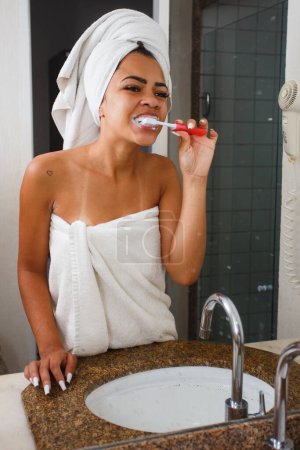 Téléchargez les photos : Afro femme brossant ses dents dans la salle de bain - en image libre de droit