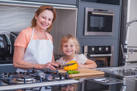Téléchargez les photos : Mère âgée et petite fille cuisinent ensemble. Mère et fille coupant des légumes pour la cuisine - en image libre de droit