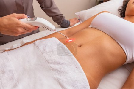 Photo for Woman making continuous and direct application of therapeutic laser on the radial artery in the belly in the spa. Woman undergoing aesthetic treatment with Ilib - Royalty Free Image