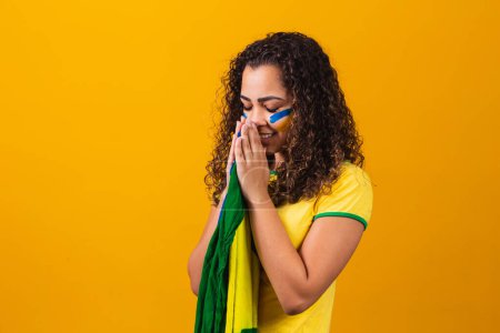Téléchargez les photos : Ventilateur brésilien avec drapeau priant sur fond jaune. prier pour le Brésil - en image libre de droit