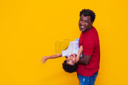 Foto de Padre e hijo afro sobre fondo amarillo sonriendo y jugando. Concepto del Día del Padre - Imagen libre de derechos