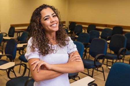 Photo for Afro student in classroom with arms crossed looking at camera smiling. Young student with the classroom in the background. - Royalty Free Image