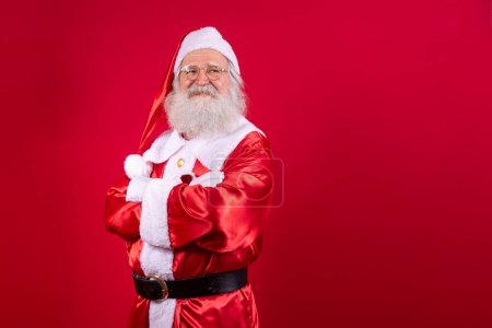 Foto de Santa Claus cruzó los brazos sobre fondo rojo. Bonito Papá Noel barbudo con los brazos cruzados sobre fondo rojo. Estudio de Santa Claus realista. - Imagen libre de derechos