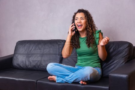 Téléchargez les photos : Jeune femme assise sur un canapé à la maison et parlant sur un téléphone portable. - en image libre de droit
