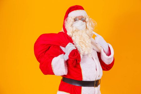 Téléchargez les photos : Véritable Père Noël sur fond jaune, portant un masque de protection contre la covid19. Noël avec distance sociale. Covid-19 - en image libre de droit