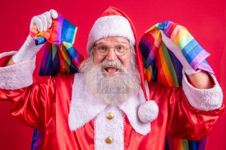 Téléchargez les photos : Le Père Noël couvre de drapeau de fierté LGBT. Tout seul. Un seul. Garder le poing levé, couvrir le drapeau LGBT. Drapeau LGBT + sur fond rouge. Noël !. - en image libre de droit