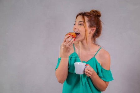 Téléchargez les photos : Jeune rousse manger des beignets et boire du thé dans le café de l'après-midi - en image libre de droit
