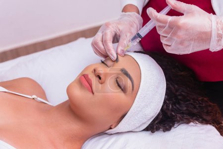 Photo for Attractive young woman is getting a rejuvenating facial injections. She is sitting quietly in the clinic. The expert beautician is filling in women's wrinkles with hyaluronic acid. - Royalty Free Image