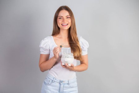 Photo for Blonde brazilian woman holding piggy bank and coin. - Royalty Free Image