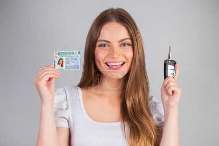 Photo for Blonde Brazilian woman holding motor vehicle driver's license and car key. Translation in English (national driver's license) - Royalty Free Image