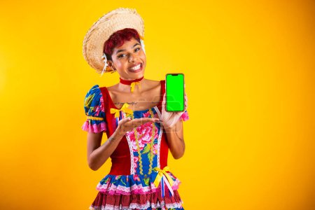 Téléchargez les photos : Femme brésilienne avec des vêtements de festa junina. Arraial, fête de Saint-Jean. montrant smartphone, avec écran vert. - en image libre de droit