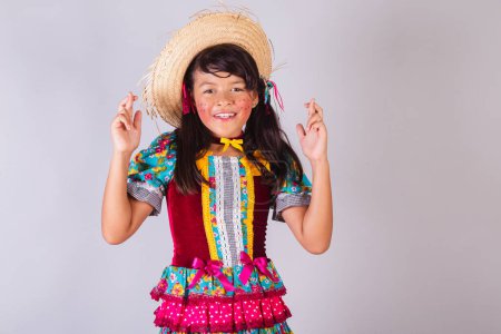 Téléchargez les photos : Enfant, fille brésilienne, avec des vêtements de festa junina, doigts croisés, souhaitant, acclamant. - en image libre de droit