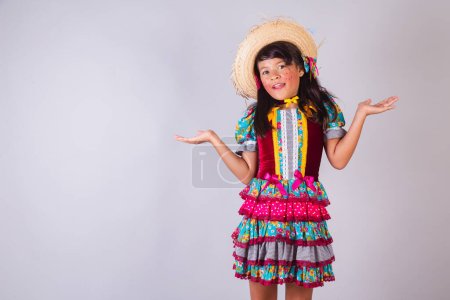 Foto de Niño, chica brasileña, con ropa de fiesta de junio, brazos abiertos, duda. - Imagen libre de derechos