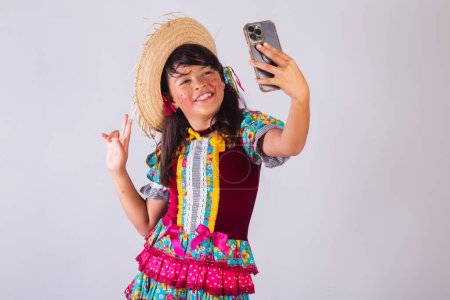 Téléchargez les photos : Enfant, fille brésilienne, avec des vêtements de fête de juin, prenant autoportrait. - en image libre de droit