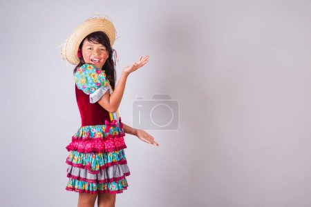 Foto de Niño, chica brasileña, con ropa de fiesta de junio, presentando algo en el lado, producto, anuncio. - Imagen libre de derechos