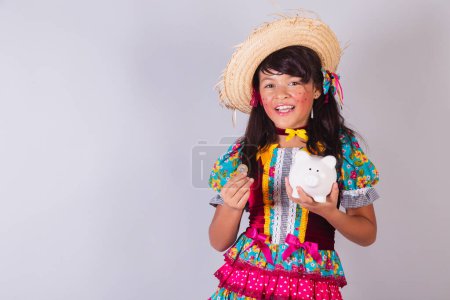 Téléchargez les photos : Enfant, fille brésilienne, dans les vêtements de la fête junina, tenant tirelire et pièce. - en image libre de droit