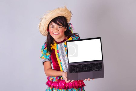 Foto de Niño, chica brasileña, con ropa de fiesta de junio, mostrando la pantalla del cuaderno. - Imagen libre de derechos