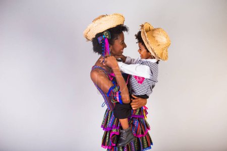 Foto de Madre e hijo afro vestidos para la fiesta de junio, fiesta brasileña llamada "Festa Junina" en celebración de So Joo. Mano en el pelo, sonriendo y abriendo los brazos. - Imagen libre de derechos