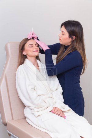 Foto de Esteticista, esteticista vistiendo bata de laboratorio, realizando un procedimiento de botox en una paciente femenina. antienvejecimiento, anti arrugas. - Imagen libre de derechos