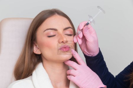 Mujer con albornoz en clínica de belleza, estética, paciente, procedimientos cosméticos. aplicación de ácido hialurónico. en los labios.