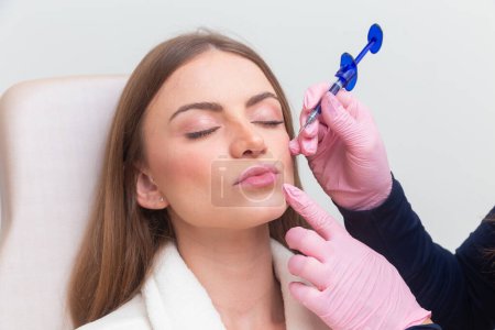 Photo for Woman wearing bathrobe in beauty clinic, aesthetics, patient, cosmetic procedures. application of hyaluronic acid. on the lips. - Royalty Free Image