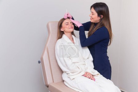 Foto de Esteticista, esteticista vistiendo bata de laboratorio, realizando un procedimiento de botox en una paciente femenina. antienvejecimiento, anti arrugas. - Imagen libre de derechos