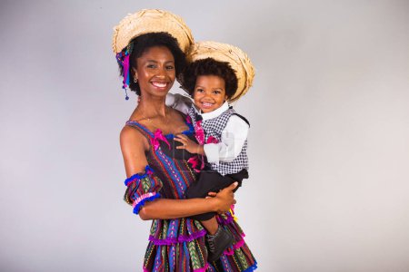 Foto de Madre e hijo afro vestidos para la fiesta de junio, fiesta brasileña llamada "Festa Junina" en celebración de So Joo. Mano en el pelo, sonriendo y abriendo los brazos. - Imagen libre de derechos