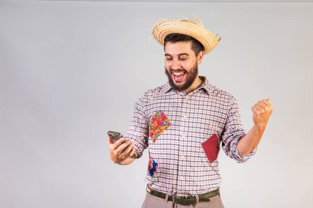 Foto de Hombre brasileño vistiendo ropa de fiesta junina. Arraial, Fiesta de San Juan. con smartphone, navegación. aplicaciones móviles. - Imagen libre de derechos