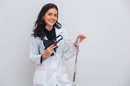 Photo for Brazilian, Caucasian woman wearing lab coat, holding tape measure for body measurement and adipometer, slimming. - Royalty Free Image