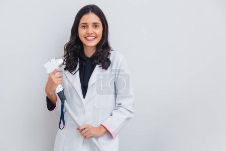 Photo for Brazilian, Caucasian woman wearing lab coat, holding laser for body and facial hair removal, laser hair removal. With firing gun. - Royalty Free Image