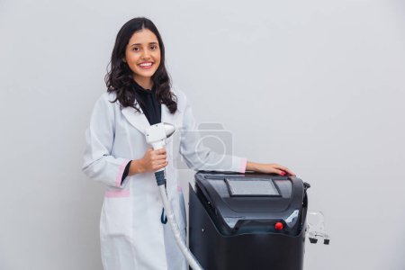 Photo for Brazilian, Caucasian woman wearing lab coat, holding laser for body and facial hair removal, laser hair removal. With pistol and machine. - Royalty Free Image