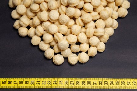 wheat, heap of round wheat snacks next to measuring tape, black background