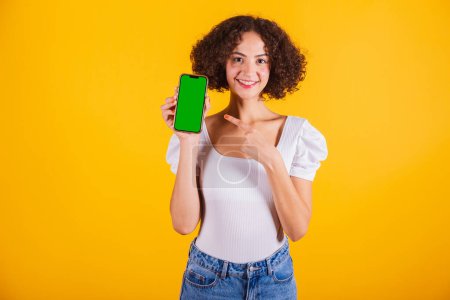 Photo for Caucasian model, wearing a white shirt and blue jeans, holding a cell phone with a green screen. - Royalty Free Image