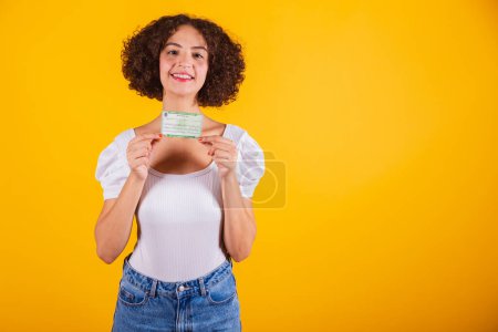 Photo for Caucasian model, in white shirt and blue jeans, holding voting card, voter registration card. translation in English (voter card) - Royalty Free Image