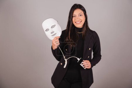 Téléchargez les photos : Femme d'affaires en costume noir. Professionnel de l'esthétique. tenant masque led. - en image libre de droit