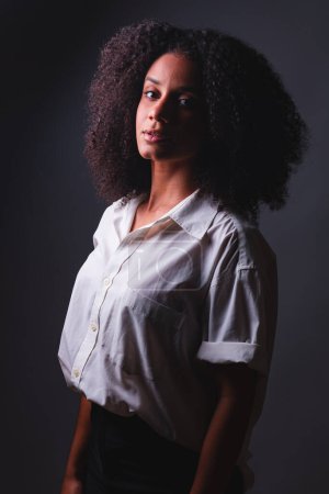 Photo for Half-body portrait, black Brazilian woman, white shirt close-up portrait, half-light photo, with marked shadow. - Royalty Free Image