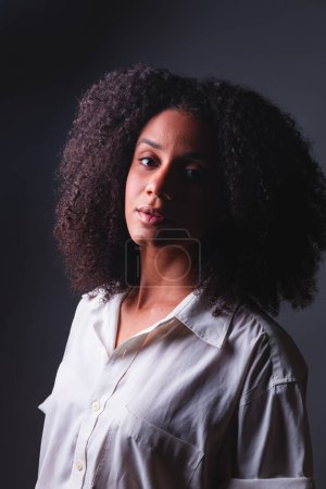 Photo for Half-body portrait, black Brazilian woman, white shirt close-up portrait, half-light photo, with marked shadow. - Royalty Free Image