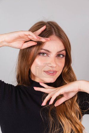 Foto de Hermosa rubia brasileña con camisa negra. foto de primer plano, posando en foto vertical con las manos a la cara. - Imagen libre de derechos