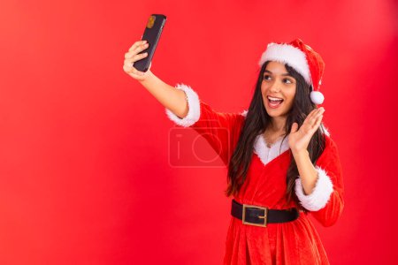 Téléchargez les photos : Femme adolescente brésilienne portant des vêtements de Noël, smartphone prenant selfie. - en image libre de droit
