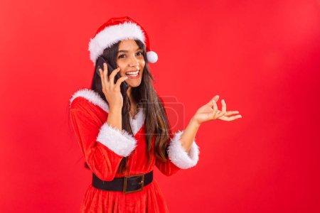 Photo for Brazilian teenage woman wearing Christmas clothes, smartphone on voice call. - Royalty Free Image
