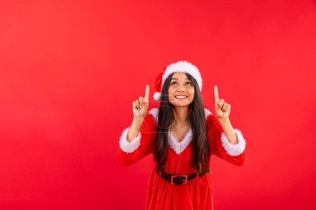 Foto de Mujer brasileña, adolescente, vestida con ropa navideña, mostrando algo arriba, espacio negativo para publicidad y anuncios. - Imagen libre de derechos
