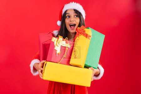 Foto de Adolescente brasileña vistiendo ropa de Navidad, sosteniendo una pila de regalos. - Imagen libre de derechos