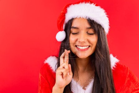 Photo for Brazilian woman, teenager, wearing Christmas clothes, close-up photo, fingers crossed wishing. - Royalty Free Image