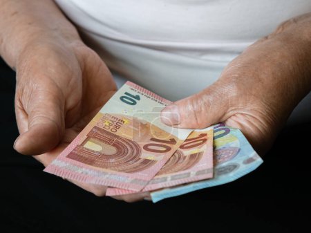 Manos de una anciana sosteniendo billetes de euro pequeños. Vista frontal
