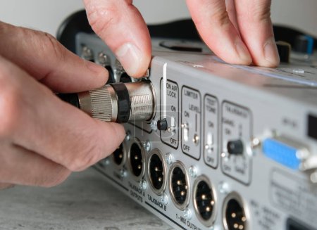 Foto de Una mano macho desconecta un cable XLR macho de la entrada de una consola de mezcla. - Imagen libre de derechos