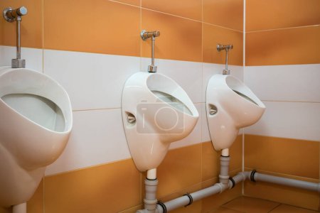 Photo for Restroom interior with white and orange ceramic tiles on the walls and a row of sanitary ware with men's urinals in a public restroom - Royalty Free Image